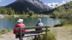 An elderly couple sitting on a bench at a lake near "Morteratsch" above the village of Pontresina in the canton of Grisons' U