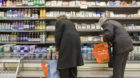 Customers study the choice of products in a cooling shelf with dairy products at the Migros branch "Puent" in Zurich-Albisrie