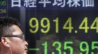 A man walks in front of the electronic stock board of a securities firm showing Japan's Nikkei 225 index fallen 135.95 points