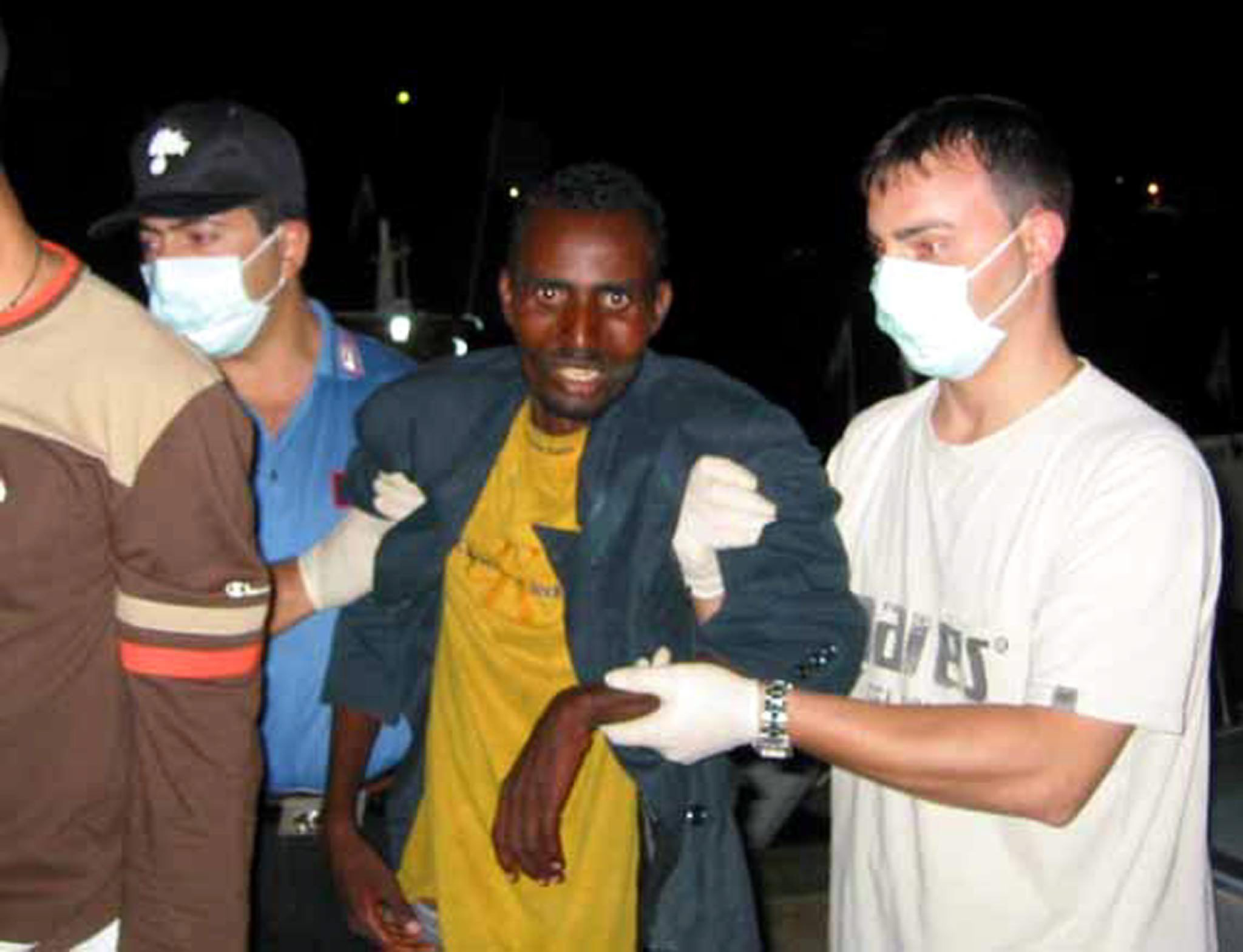 Italienische Carabinieri begleiten einen Somalier, der in Lampedusa landete. Zu ihrem Schutz tragen sie Handschuhe und Mundschutz.