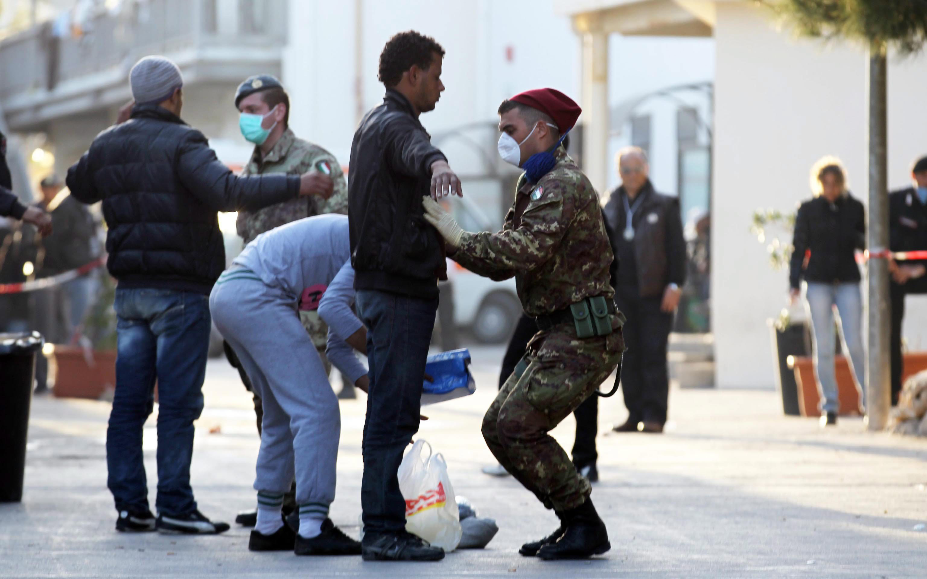 Körperkontrolle in Lampedusa: Die staatliche Autorität zeigt sich in Uniform, mit Schutzvorkehrungen.