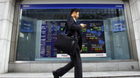 A man uses a smartphone near an electronic stock board outside a securities company in Tokyo, Friday, Oct. 3, 2014. Tokyo's N