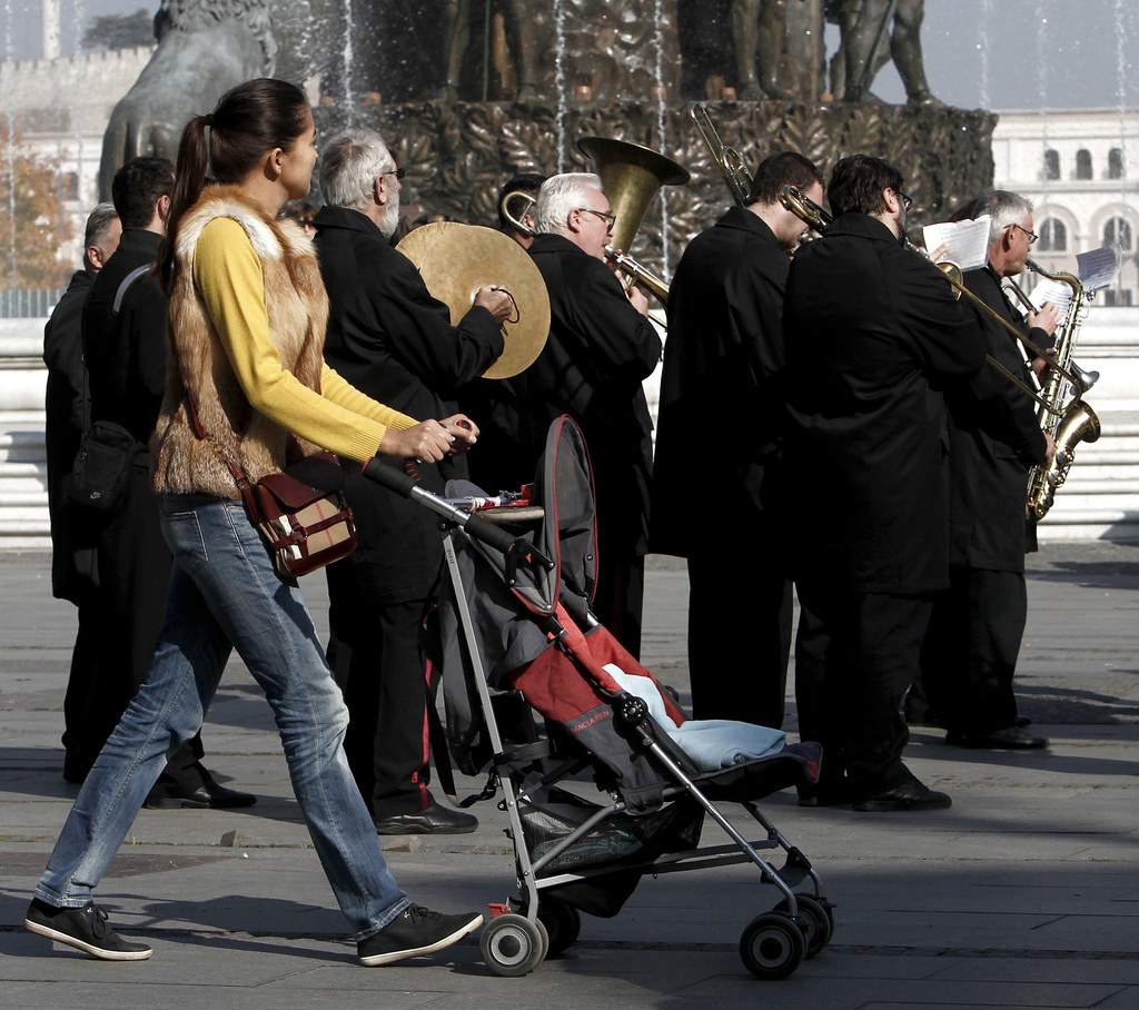 A young woman, pushing a baby carriage, passes by a band playing in Skopje, Macedonia, Sunday, Nov. 2, 2014. According to the local authorities, the number of foreign tourists visiting Skopje is increasing every year. (AP Photo/Boris Grdanoski)