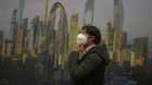 epa04495198 A man adjusts his mask to protect against smog beside a billboard featuring an artist impression of clear weather