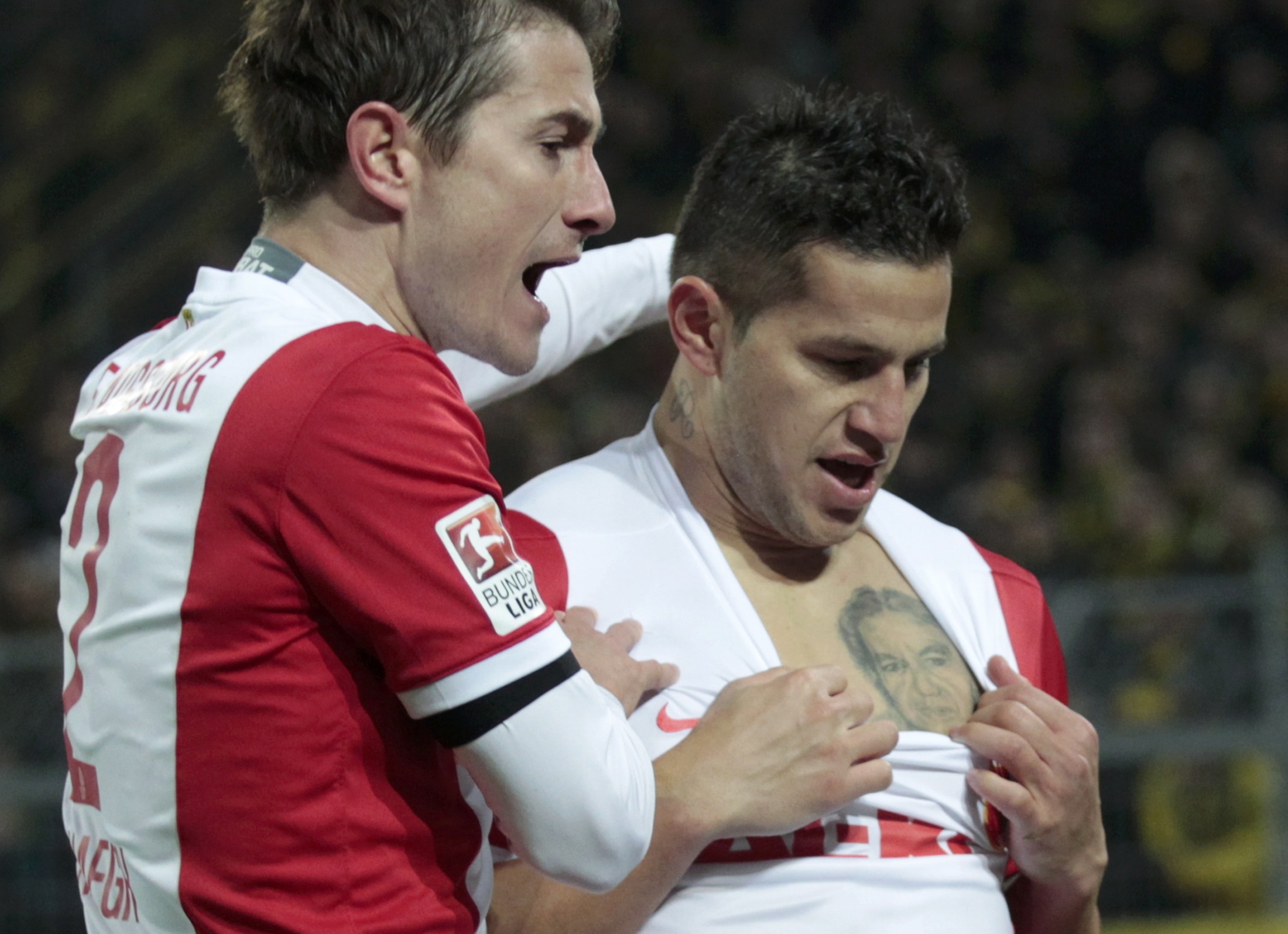 FC Augsburg's Raul Bobadilla shows his tatoo and celebrates his goal against Borussia Dortmund with fellow team mate Paul Verhaegh during their German first division Bundesliga soccer match in Dortmund February 4, 2015. REUTERS/Ina Fassbender (GERMANY - Tags: SPORT SOCCER) DFL RULES TO LIMIT THE ONLINE USAGE DURING MATCH TIME TO 15 PICTURES PER GAME. IMAGE SEQUENCES TO SIMULATE VIDEO IS NOT ALLOWED AT ANY TIME. FOR FURTHER QUERIES PLEASE CONTACT DFL DIRECTLY AT + 49 69 650050.