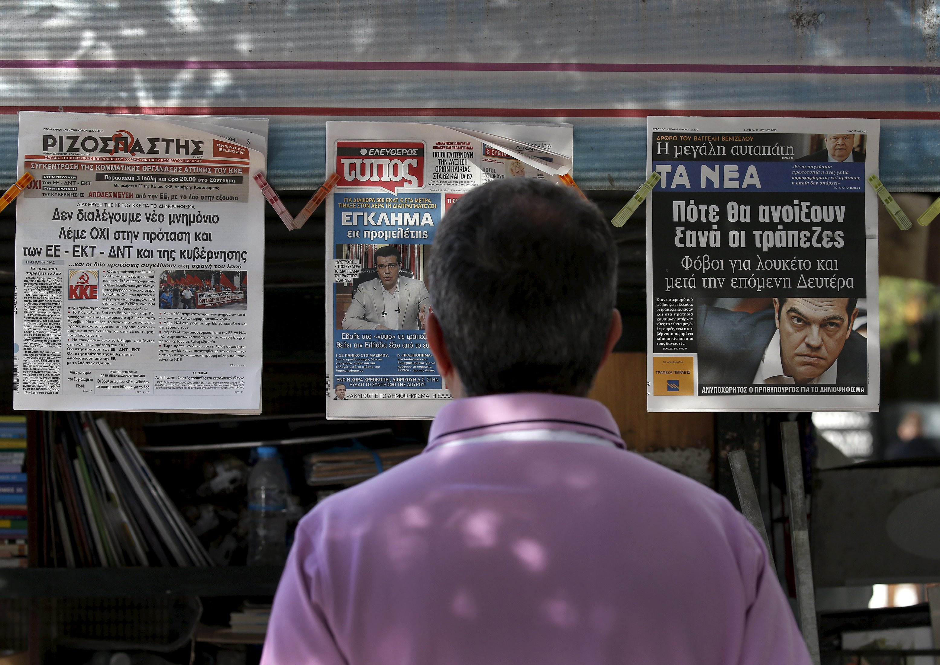 A man reads the front pages of various newspapers hanging at a kiosk in Athens, Greece June 29, 2015. Greece closed its banks and imposed capital controls on Sunday to check the growing strains on its crippled financial system, bringing the prospect of being forced out of the euro into plain sight. REUTERS/Yannis Behrakis