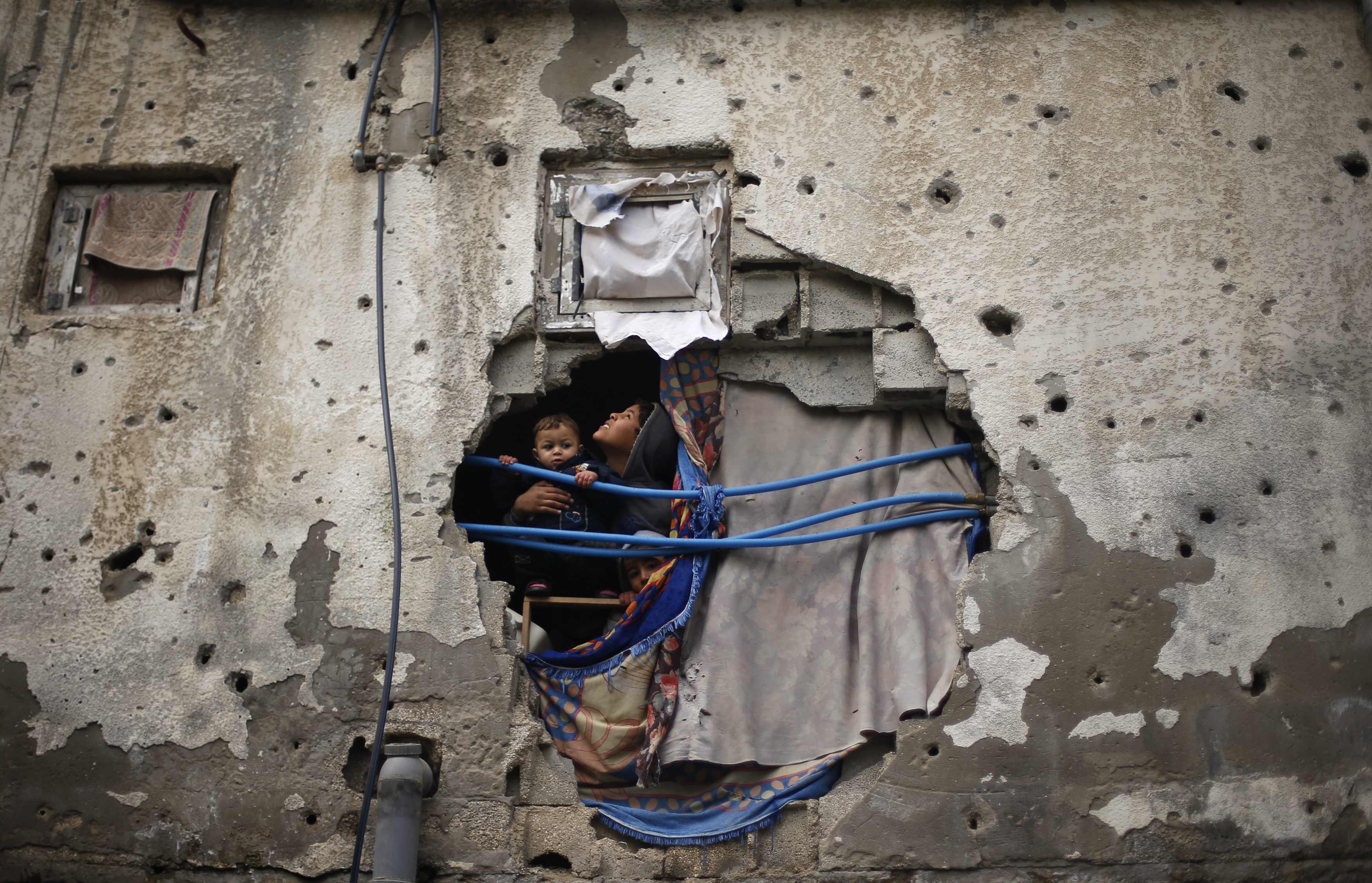 Palestinian children look out through a hole covered with a blanket in their family house, that witnesses said was damaged by Israeli shelling during a 50-day war last summer, in the east of Gaza City January 7, 2015.