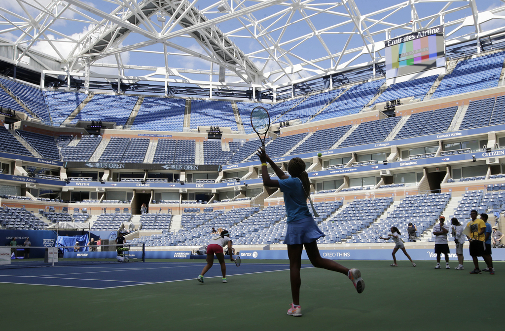 Youngsters hit to each other as they stand in for some of the U.S. Open tennis tournament's top seeds on Arthur Ashe court during a rehearsal for Arthur Ashe Kids' day at the USTA Billie Jean King National Tennis Center in New York, Thursday, Aug. 27, 2015. The framework for a partially-complete retractable roof, visible here, will provide shade for fans, but rain delays could still plague the two-week long sporting event. (AP Photo/Kathy Willens)