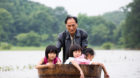 A man pushes a tub carrying children as he gets them back home after school at a flooded area in Duchang, Jiangxi Province, C