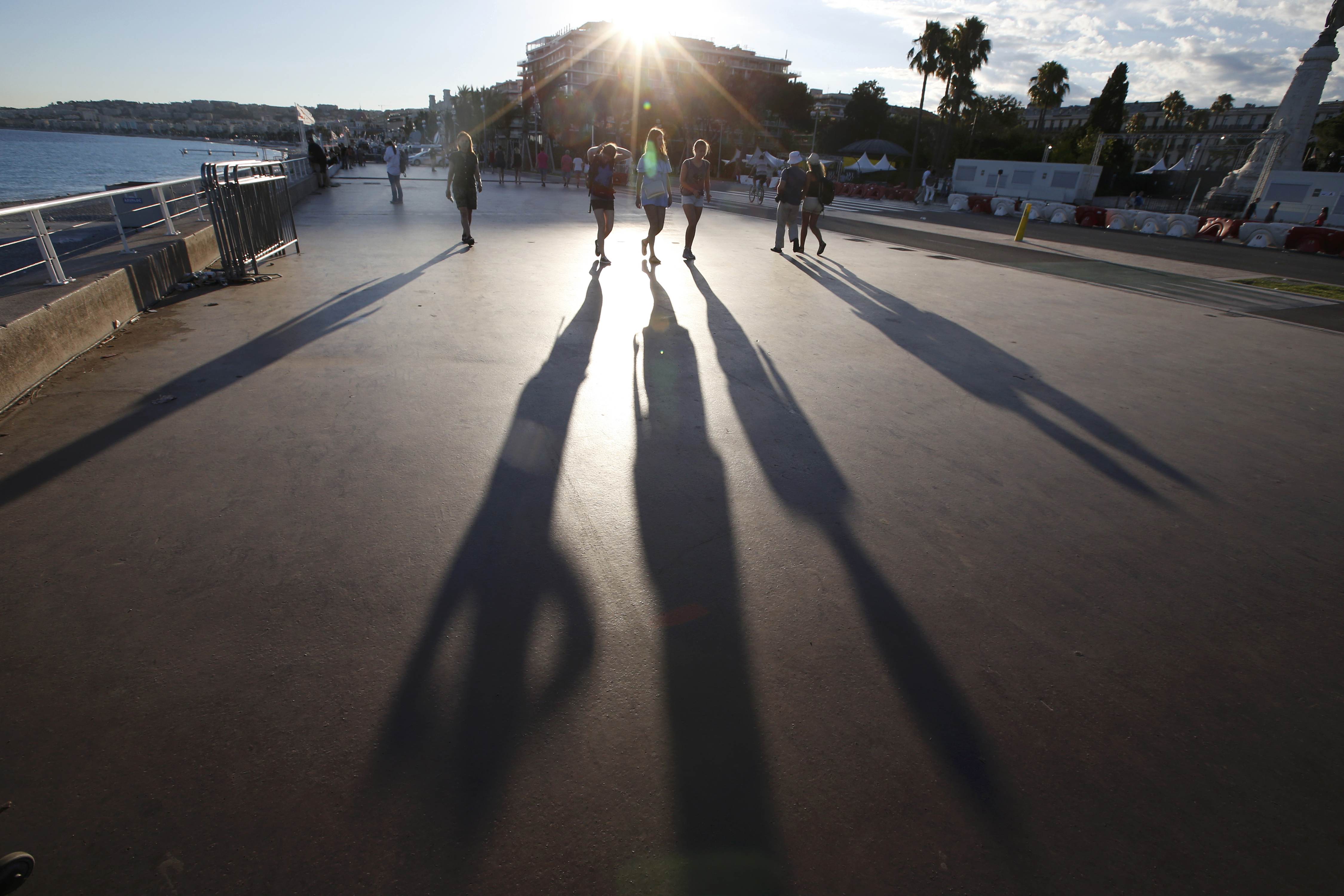 The sun casts long shadows as people walk on the Promenade des Anglais the day after a truckran into a crowd at high speed killing scores and injuring more who were celebrating the Bastille Day national holiday, in Nice, France, July 15, 2016. REUTERS/Eric Gaillard