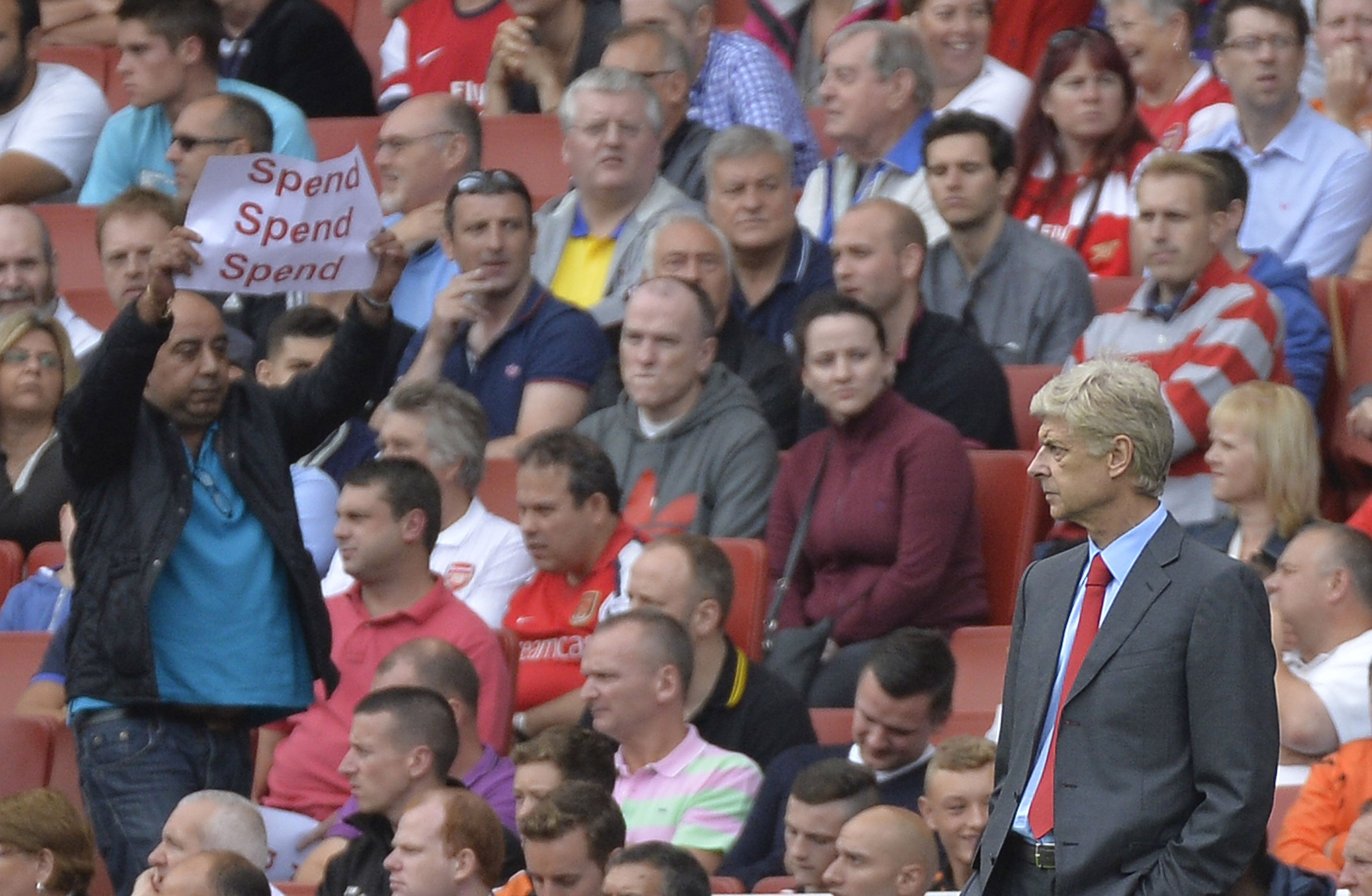 A fan holds a protest banner (L) as Arsenal's manager Arsene Wenger watches during their English Premier League soccer match against Aston Villa at Emirates Stadium in London August 17, 2013. REUTERS/Toby Melville (BRITAIN - Tags: SPORT SOCCER) NO USE WITH UNAUTHORIZED AUDIO, VIDEO, DATA, FIXTURE LISTS, CLUB/LEAGUE LOGOS OR 