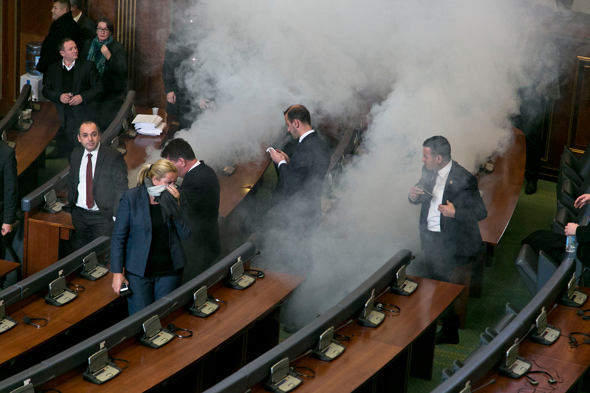 Lawmakers react as opposition lawmakers release tear gas canisters disrupting a parliamentary session in Kosovo capital Pristina on Monday Dec. 14, 2015. Opposition lawmakers have released tear gas in Kosovo’s parliament in their latest attempt to pressure the government into renouncing deals with Serbia and Montenegro. Clouds of smoke at the debating chamber released from two smuggled tear gas canisters forced lawmakers out of parliament Monday, something the opposition has successfully achieved since mid-September also using pepper spray, whistles and water bottles. (AP Photo/Visar Kryeziu)