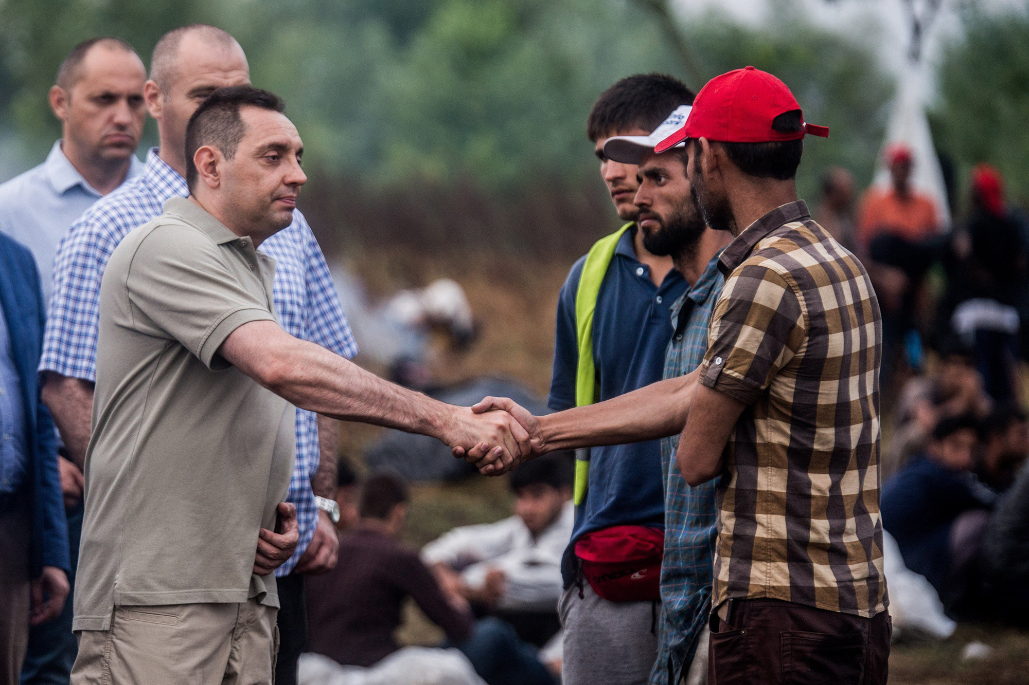 Serbian Minister of Social Affairs Aleksandar Vulin, left, shakes hands with migrants who are on hunger strike in an effort to put pressure on the Hungarian government to open the national border, sit at the border between Serbia and Hungary at Horgos, Northern Serbia, Tuesday, July 26, 2016. There are around 1,400 migrants staying in Northern Serbia waiting for the opportunity to continue their journey to central Europe, but the border remains closed. (Zoltan Balogh/MTI via AP)